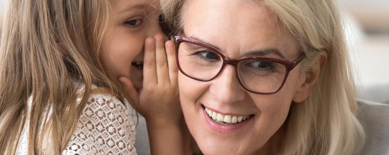 child whispering into grandma's ear